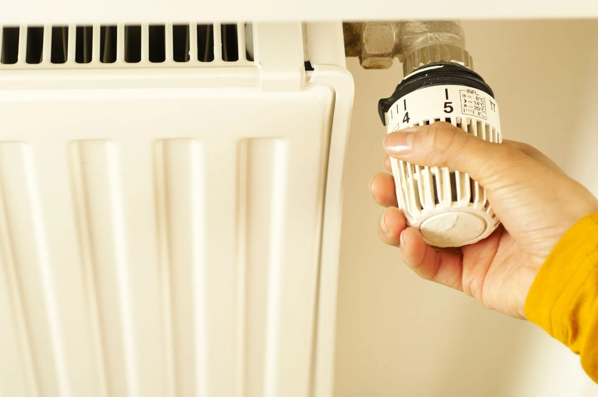 A hand turning a thermostatic valve on a radiator