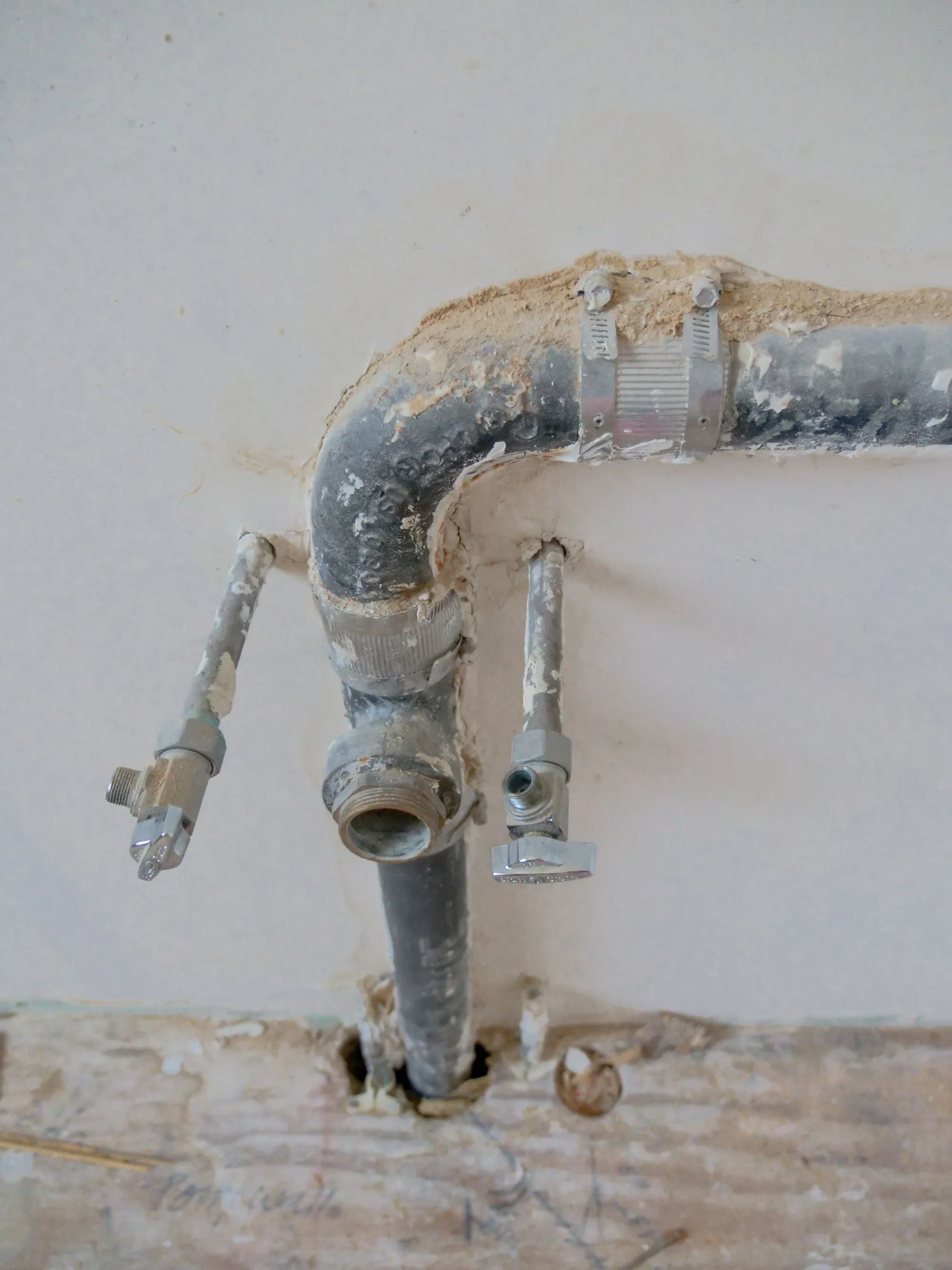Old galvanized pipe in an opened wall, patched with a hose clamp