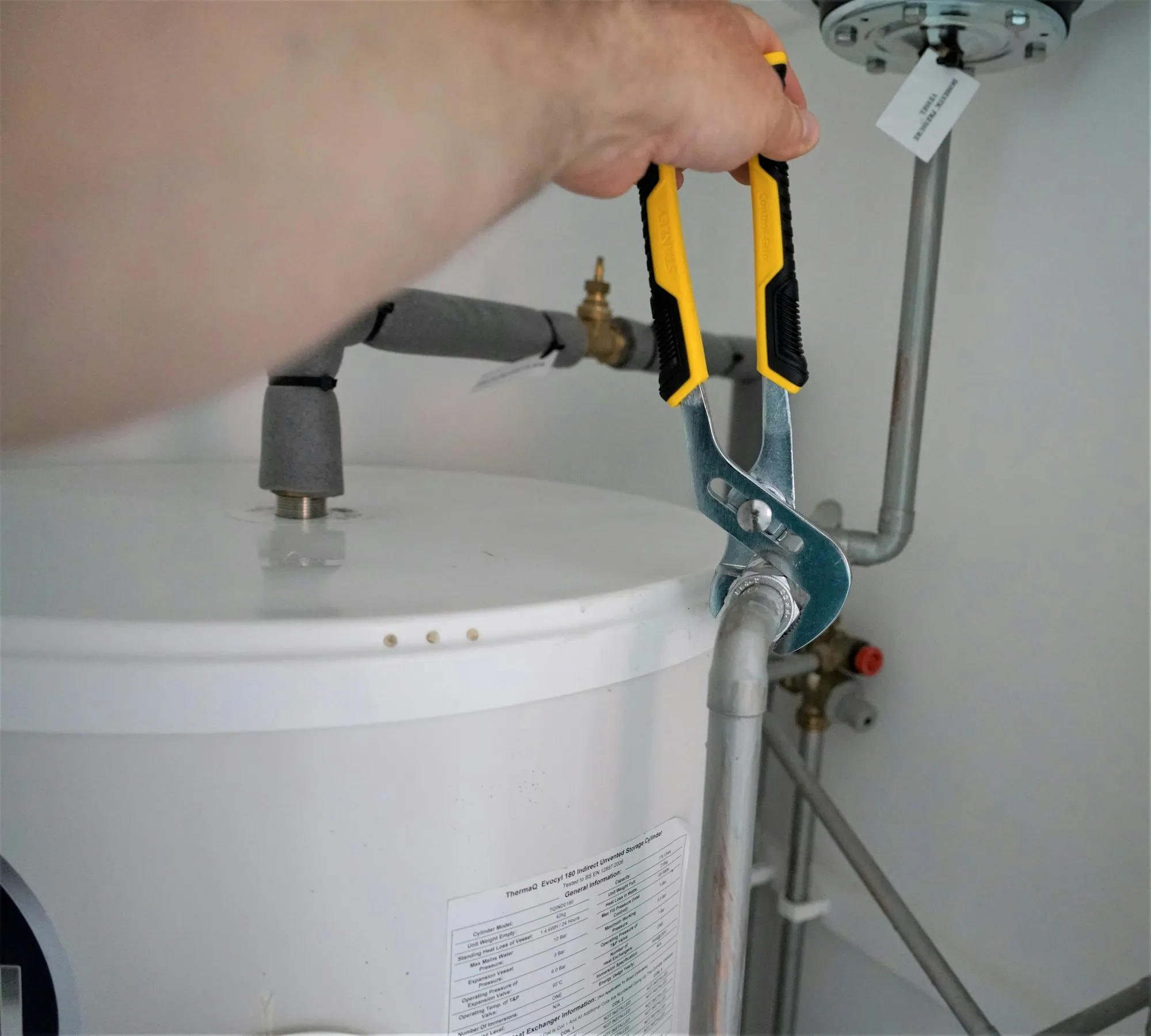 Pliers tightening the supply connection on top of a new white tank water heater